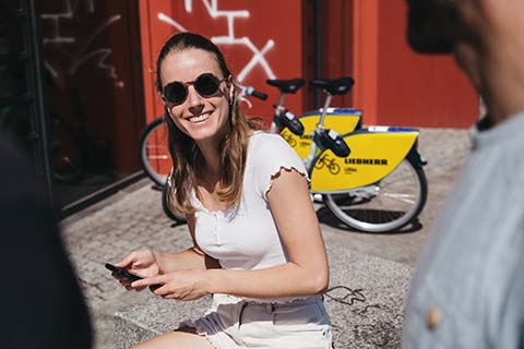 Eine junge Frau schaut eine weitere Person im Vordergrund an, im Hintergrund steht ein nextbike Leihrad